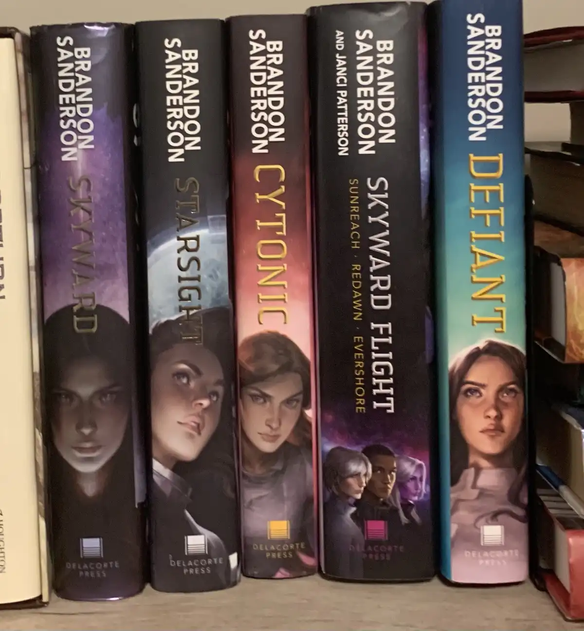 Five books from Brandon Sanderson's 'Skyward' series are shown standing upright on a shelf, their spines visible. From left…