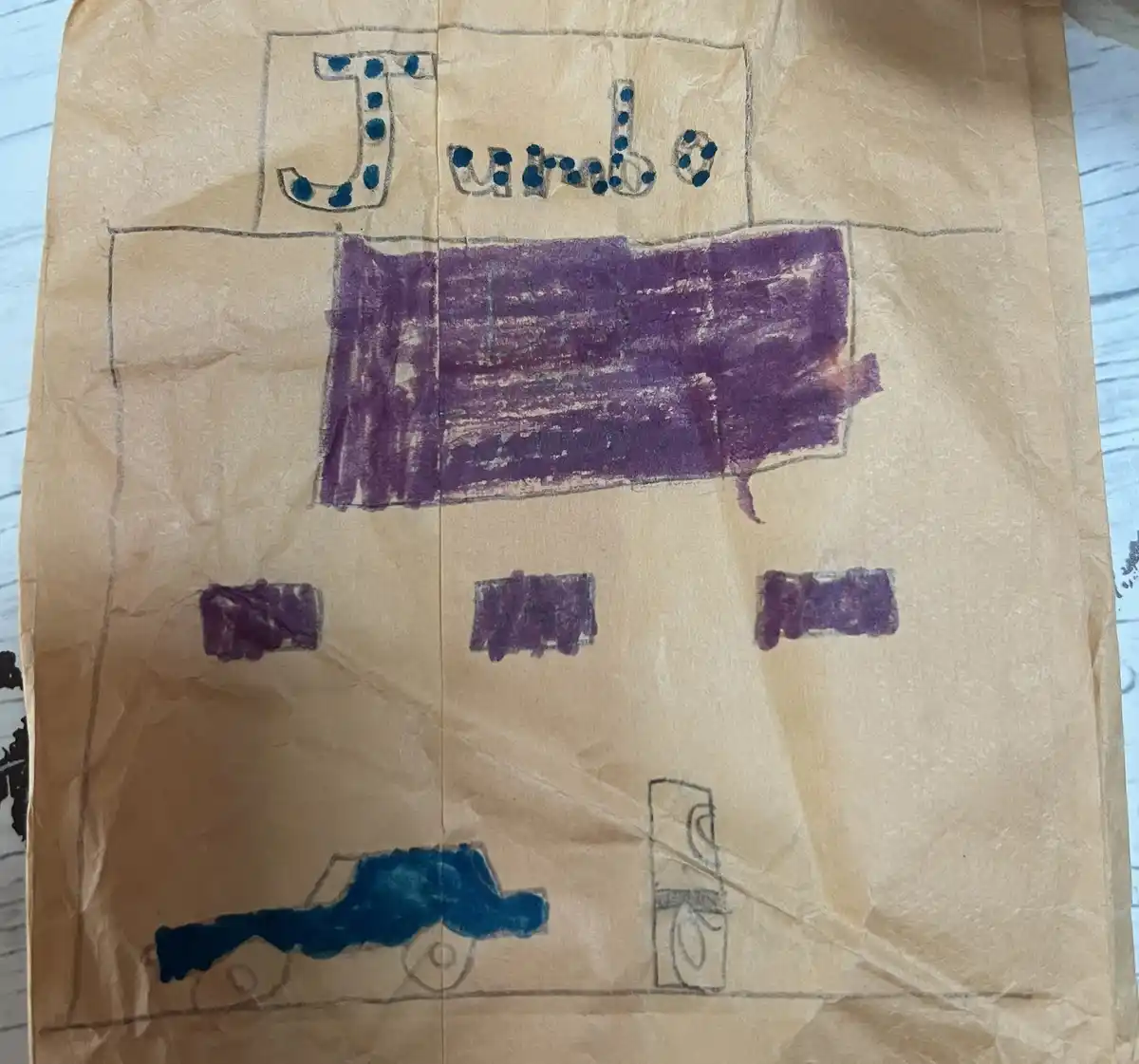 A child's drawing on a brown paper bag shows a large truck labeled 'Jumbo' with purple crayon boxes and a blue truck below…