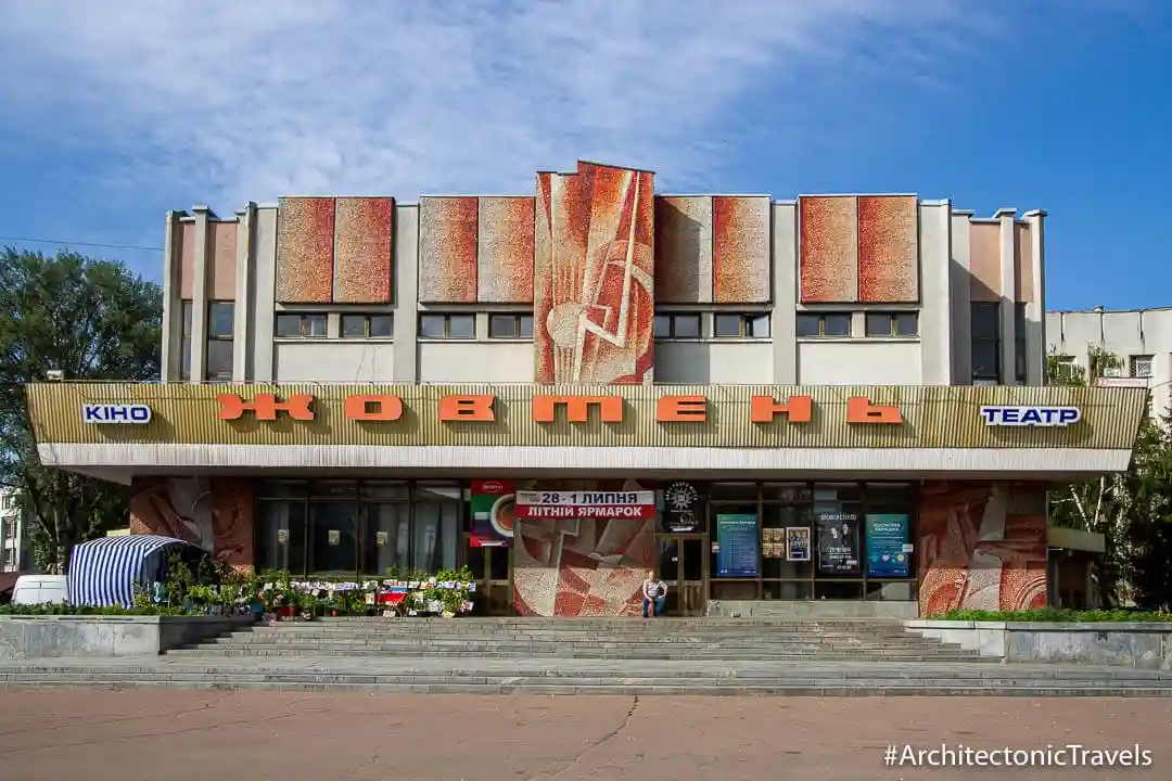 A wide-angle photo of a Soviet-era cultural center building with large orange Cyrillic letters spelling 'жовтень' across the…