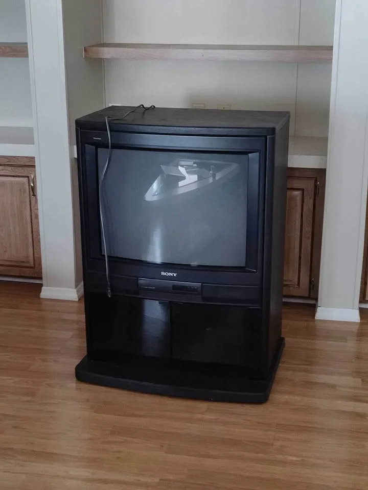 A black Sony CRT television sits on a wooden floor in a room with built-in shelving and cabinets. The TV screen is off and…