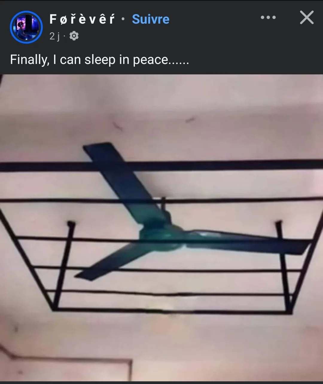 A ceiling fan is shown with its blades completely enclosed within a black metal safety cage, which is mounted to the…
