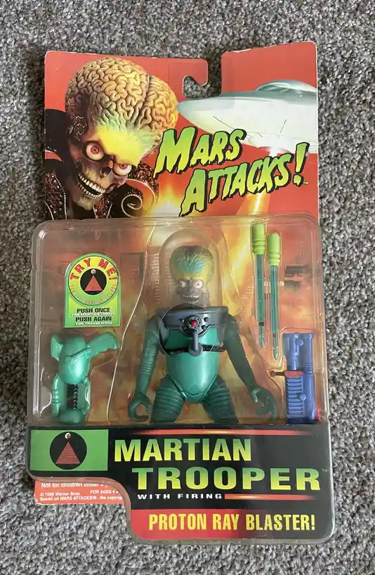 A vintage 'Mars Attacks!' Martian Trooper action figure in its original blister pack, featuring a green-skinned alien with a…