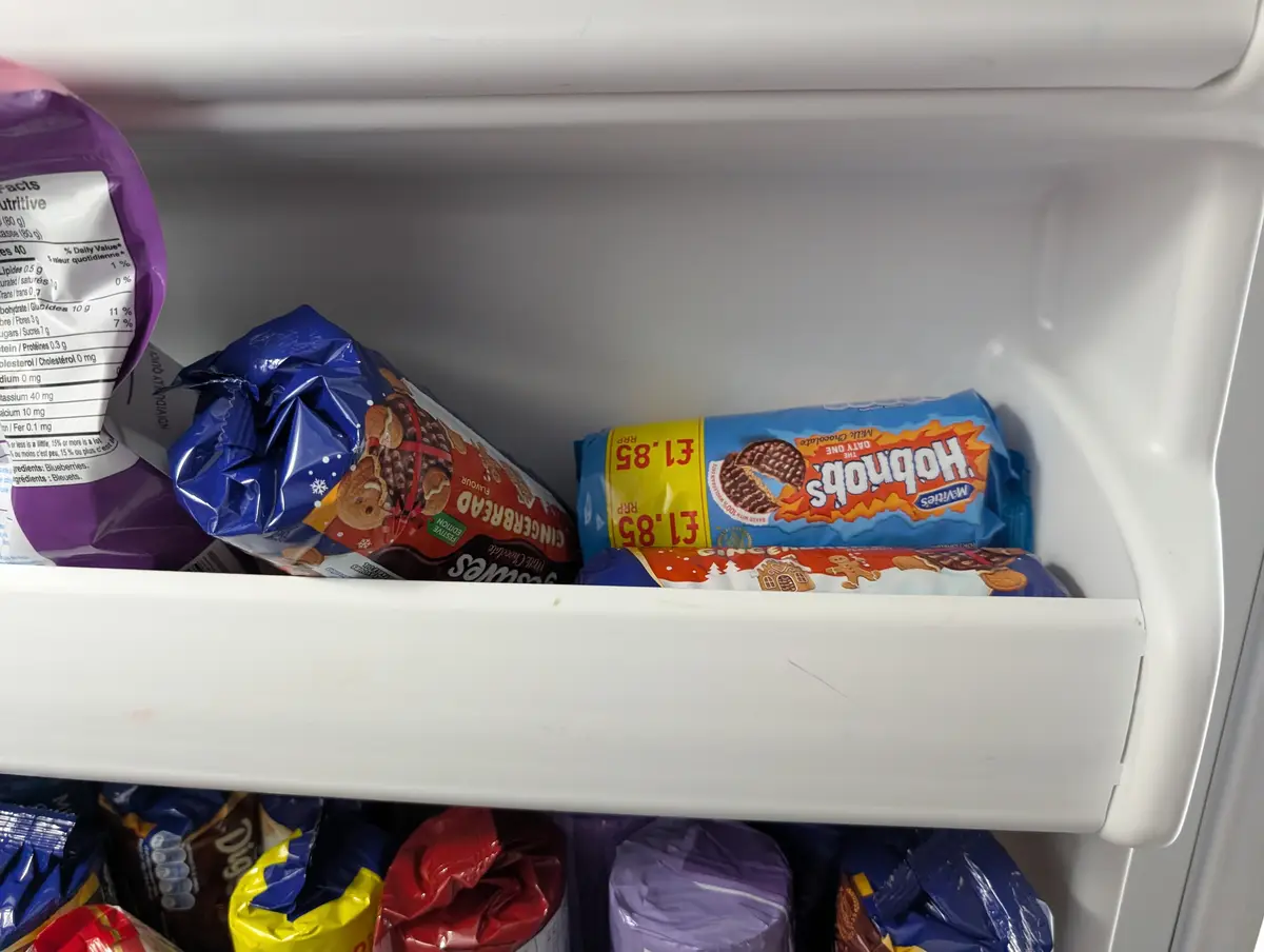 A close-up shot of a refrigerator shelf filled with various bags of biscuits and snacks, including a blue bag of McVitie's…