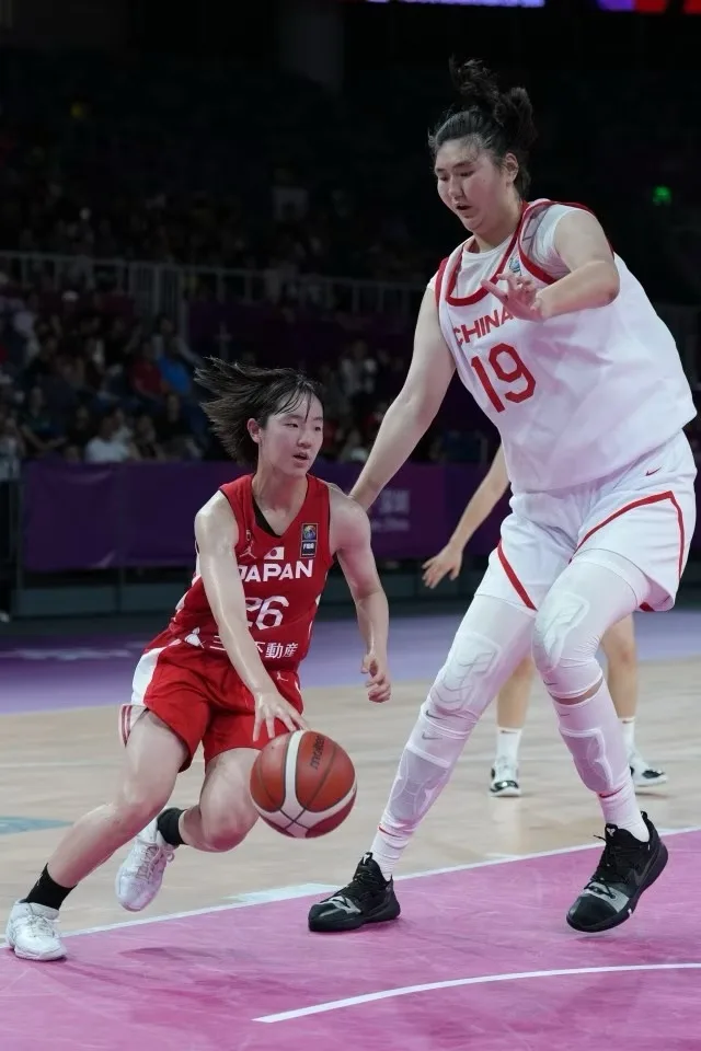 一名身穿红色球衣、印有“JAPAN”和号码“26”的日本女篮球员正在运球突破，她面前是一名身穿白色球衣、印有“CHINA”和号码“19”的中国女篮球员正在防守。中国球员身体前倾，手臂伸展试图封堵，日本球员则低重心带球前进，背景是篮球场和观众席。图像上…