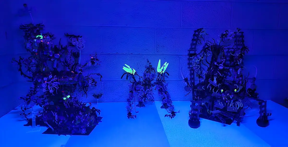 A photo of intricate Lego Ninjago builds illuminated under blacklight, causing glowing green elements to stand out against a…