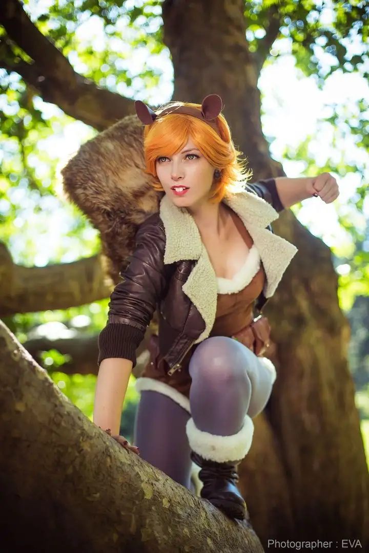 A person in a cosplay outfit with orange hair, brown ears, and a large furry tail is crouching on a tree branch in a forest…
