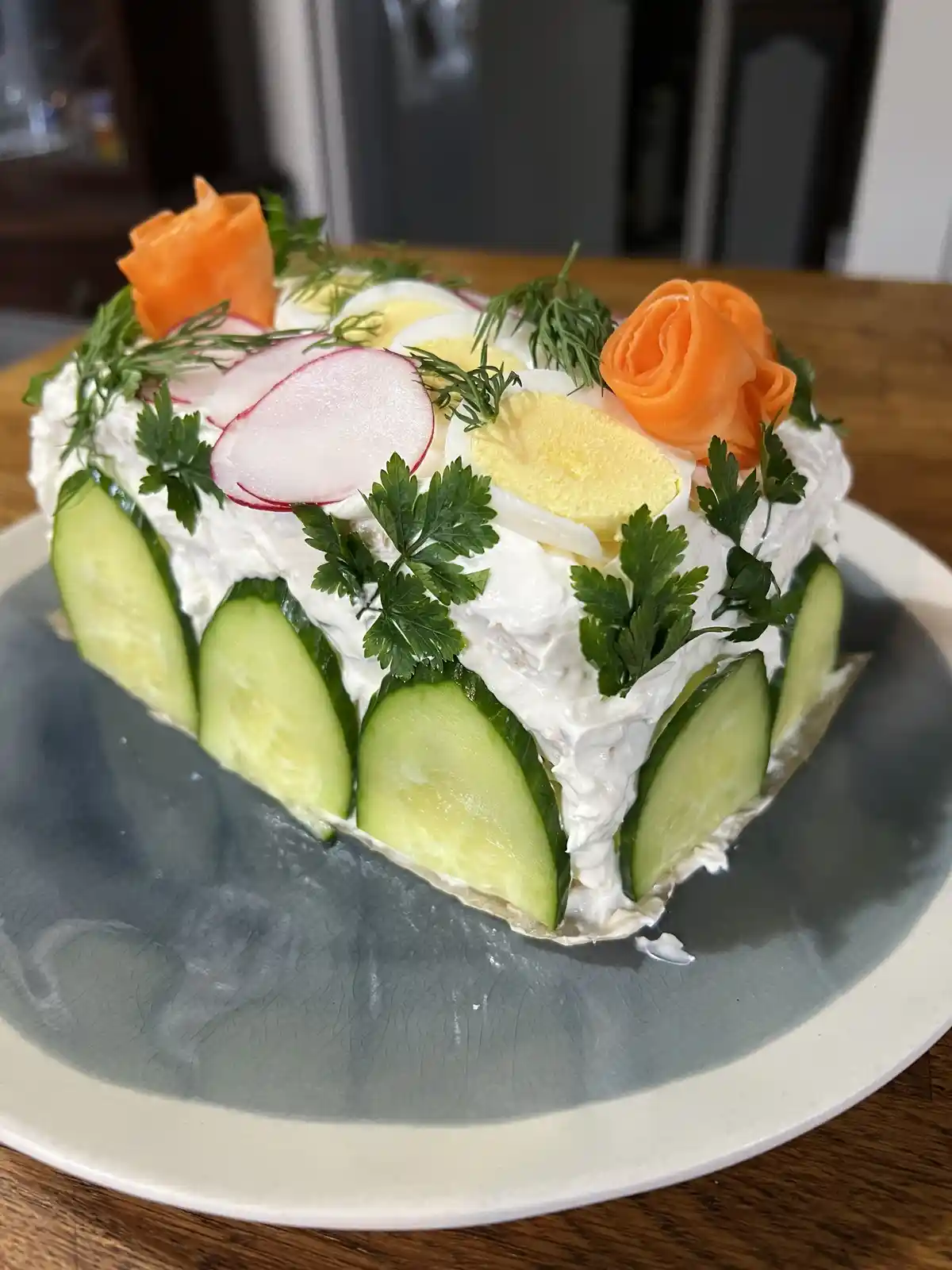A heart-shaped dish covered in white cream, decorated with sliced cucumbers around the base, radish slices, boiled egg…