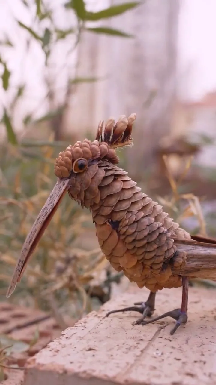 A whimsical, handcrafted bird sculpture made entirely from pinecones, featuring a long beak, detailed eye, and feather-like…
