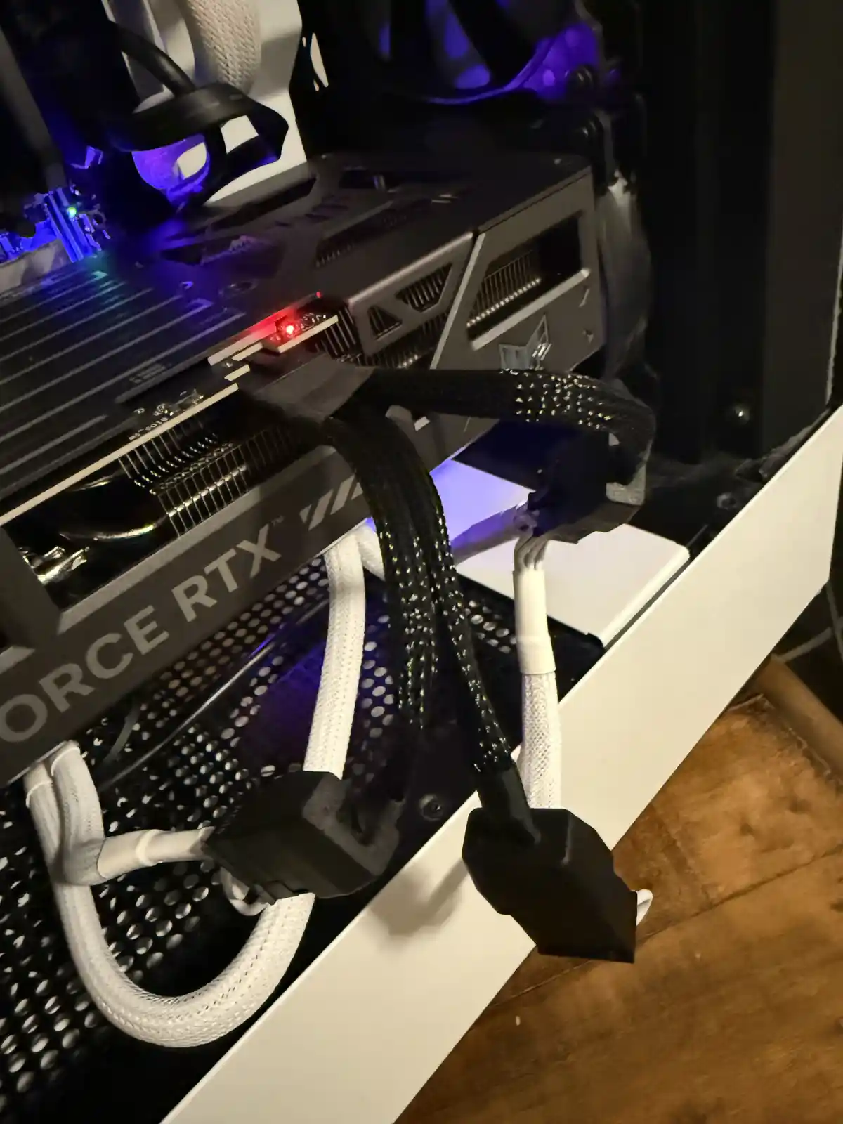 A close-up shot of a black Nvidia GeForce RTX 4090 graphics card installed in a white computer case, with its power cables…