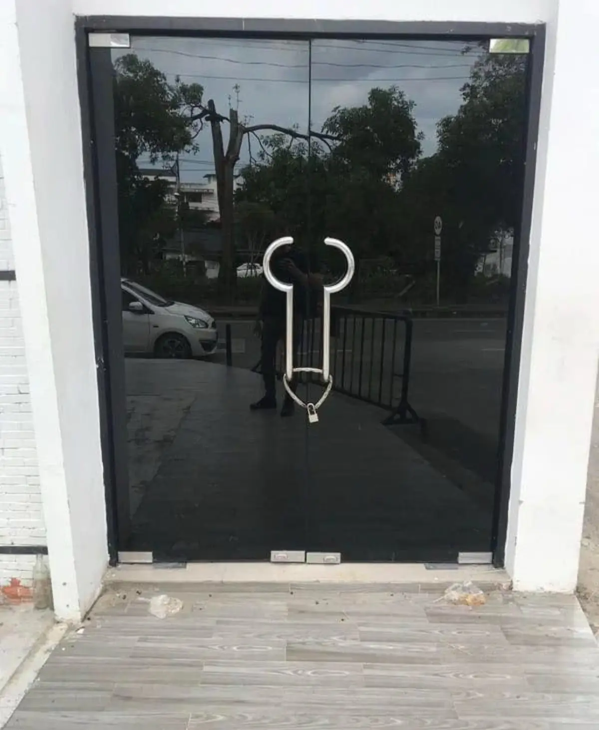 a black glass door with a large silver handle shaped like a bull's head, secured with a padlock, reflects a person taking…