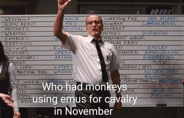 A man in a white shirt and tie stands in front of a whiteboard filled with handwritten monster and department names like…