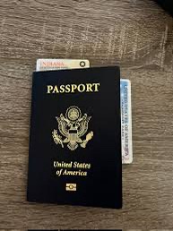 A United States passport book lies on a wooden surface, partially obscuring a credit card and a small white card with…