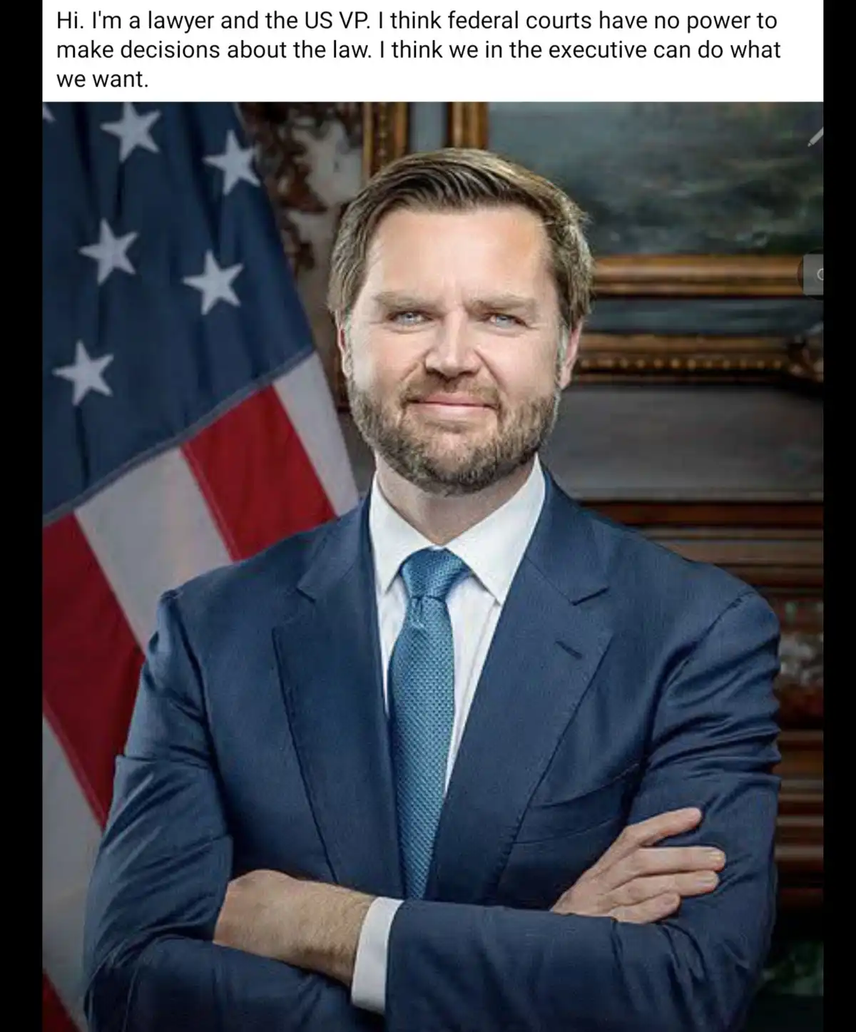 A man in a dark blue suit and blue tie stands with arms crossed in front of an American flag, smiling confidently. The…