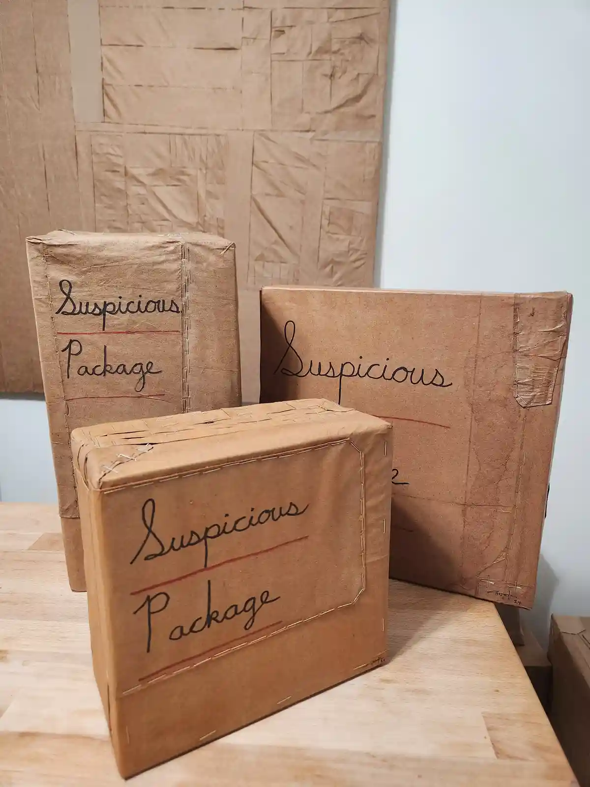 Three handmade cardboard packages, wrapped in brown paper and stitched together with visible thread, sit on a wooden…