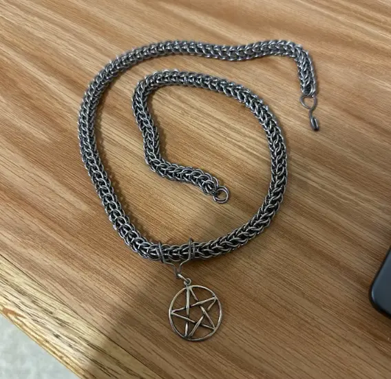A silver-colored chain necklace with a pentagram pendant lies coiled on a wooden surface. The overlaid text reads: 'i'm not…