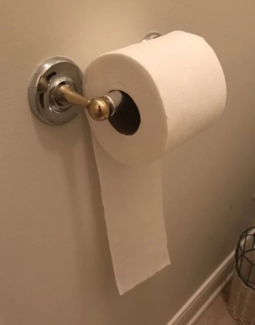 A close-up photo of a toilet paper roll on a chrome wall-mounted holder with a brass knob, showing a partially used roll and…