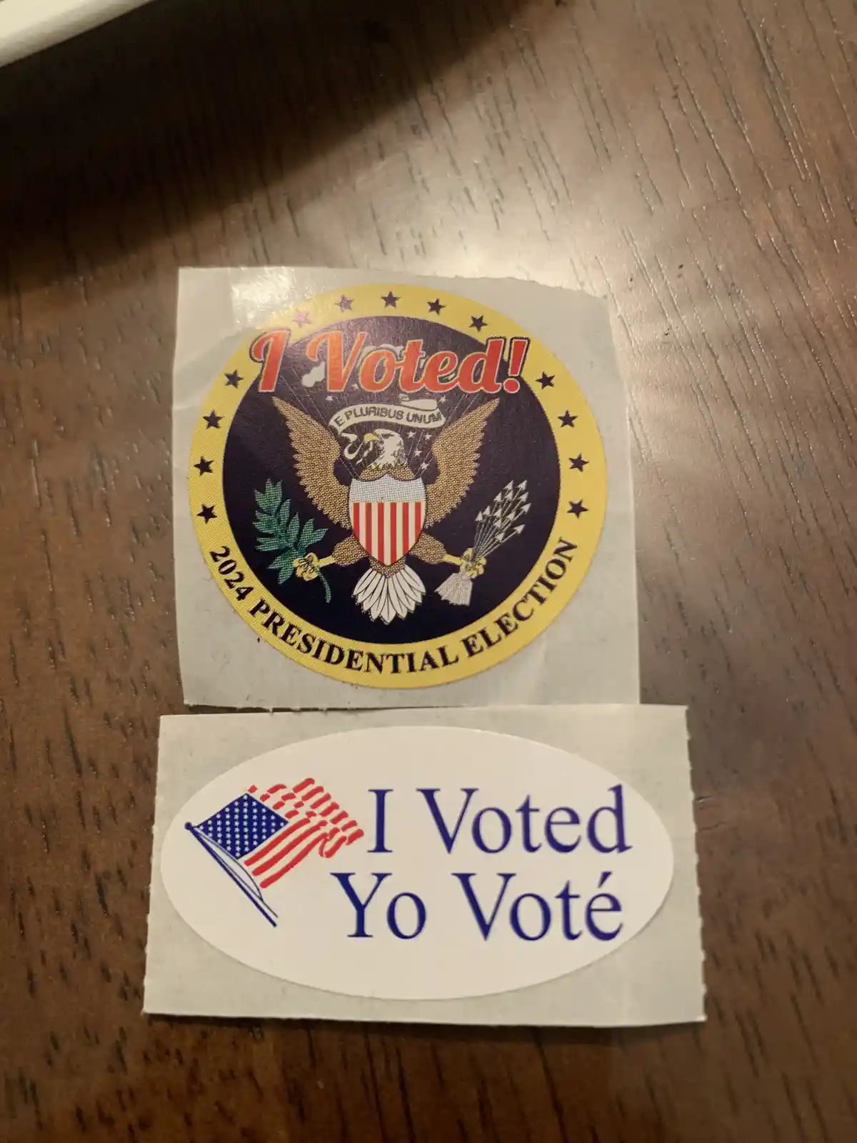 Two U.S. election stickers lie on a wooden surface: a circular 'I Voted!' sticker for the 2024 Presidential Election…