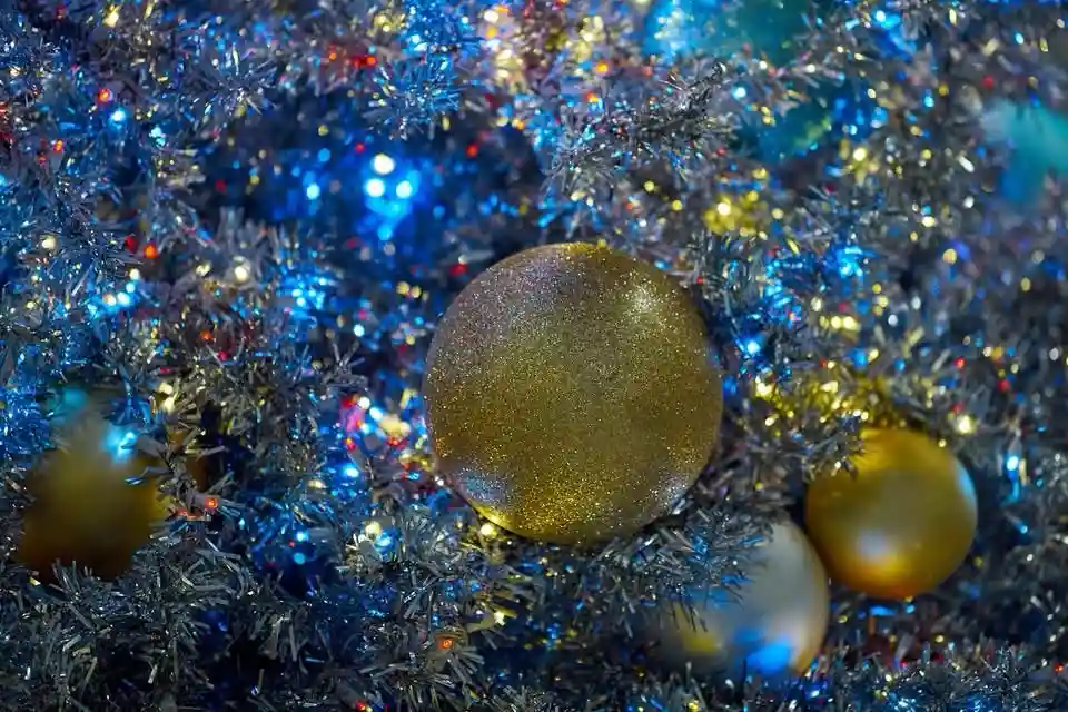 A close-up photo of a glittery gold Christmas ornament nestled among blue and silver tinsel with blurred lights in the…