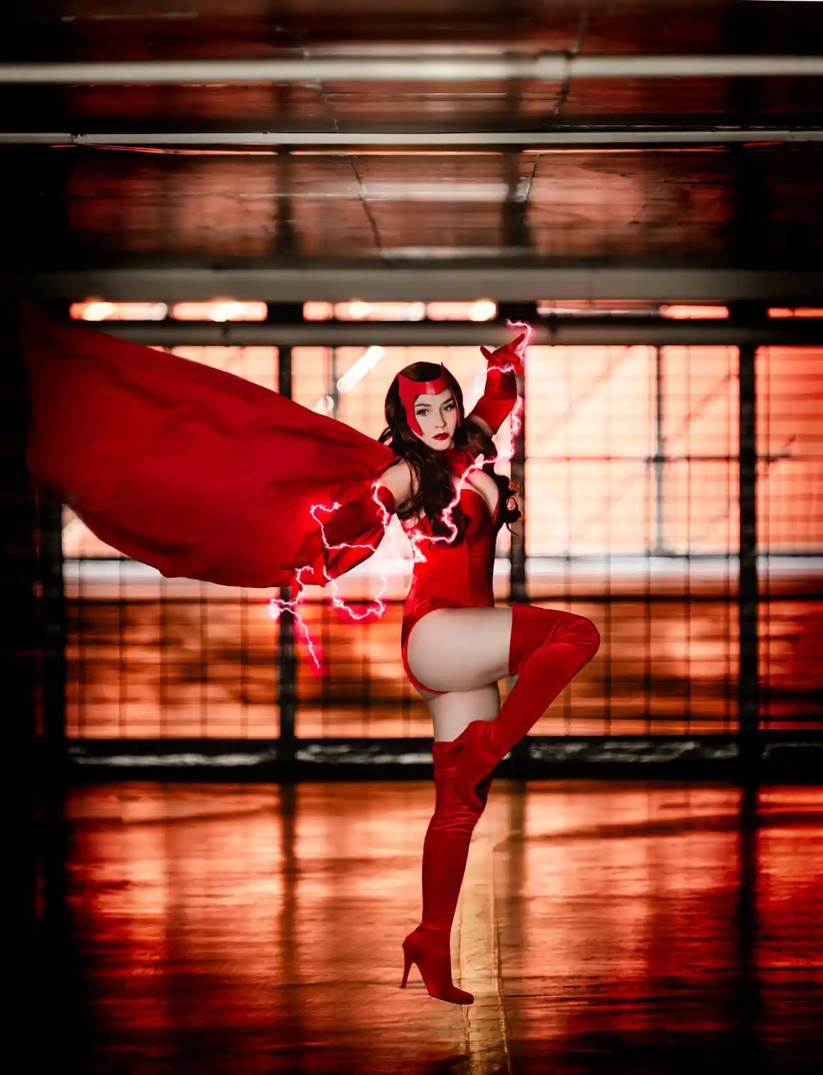 A woman in a full red superhero costume, complete with cape, gloves, and high-heeled boots, strikes a dynamic pose with…