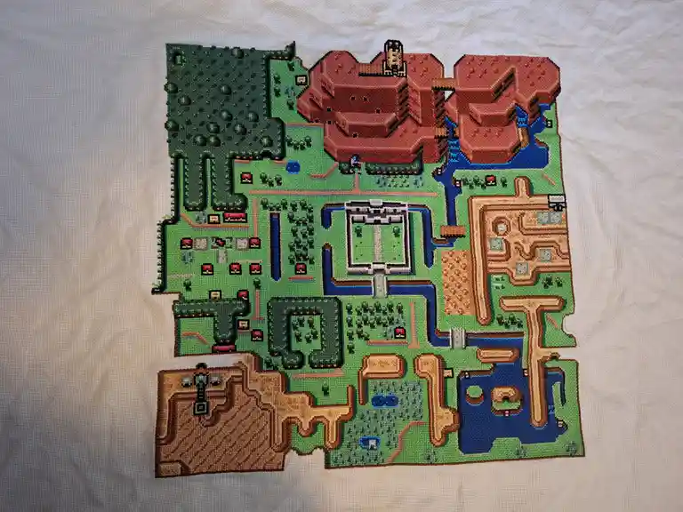 a cross-stitch artwork depicting the pixelated map of the game zelda: breath of the wild, stitched onto a white fabric…