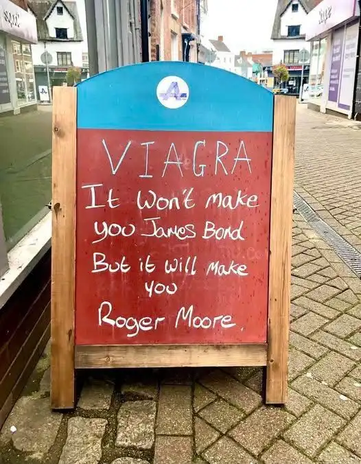 A red and blue wooden A-frame sign on a sidewalk displays handwritten text advertising Viagra, humorously claiming it won't…