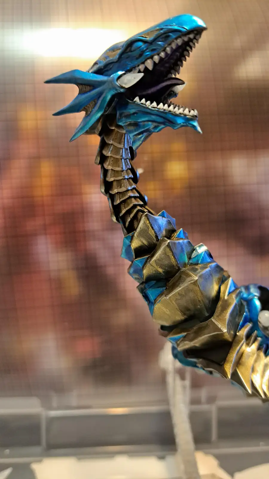 A close-up photo shows a detailed blue and gold dragon figurine with an open mouth full of sharp teeth and a spiky crest…