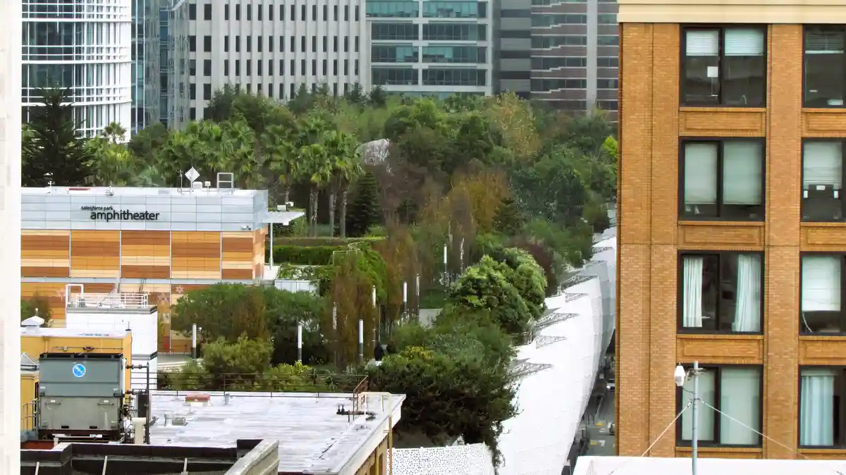 An urban rooftop view shows a building labeled 'salesforce park amphitheater' with orange and beige panels, surrounded by…