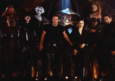 A promotional still from the movie 'The Matrix' featuring the main cast standing in a dark, futuristic setting with glowing…