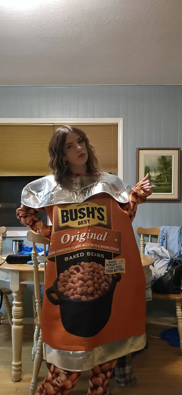 A person is dressed in a full-body costume resembling a Bush's Best Original Baked Beans can, complete with foil-like…