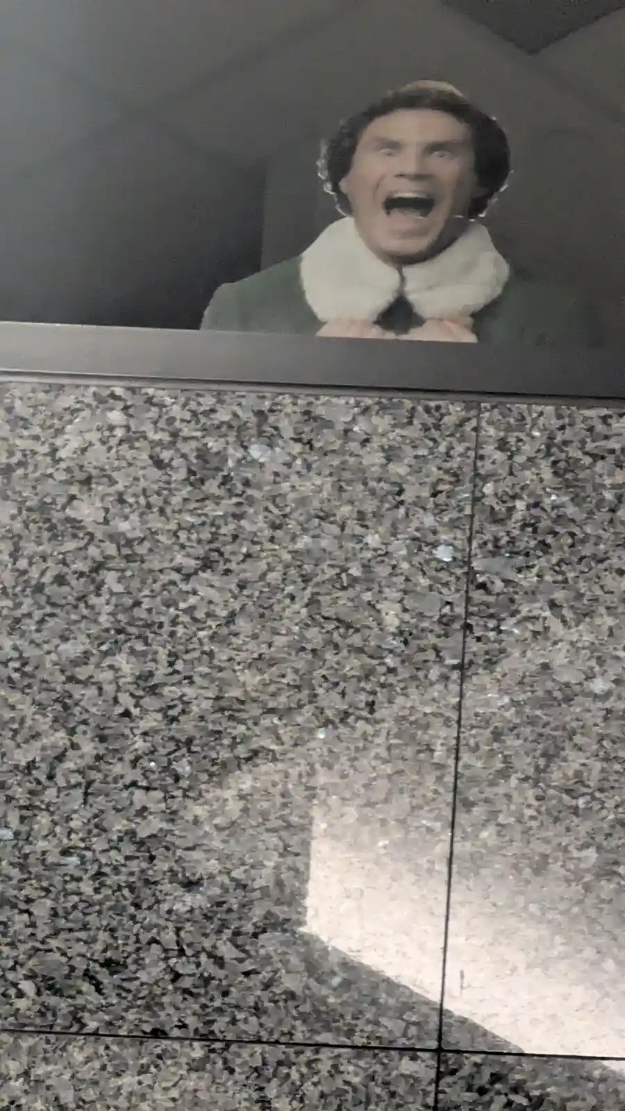 A photo shows a large, framed image of the character Buddy from 'Elf' (played by Will Ferrell) with a wide, yelling…