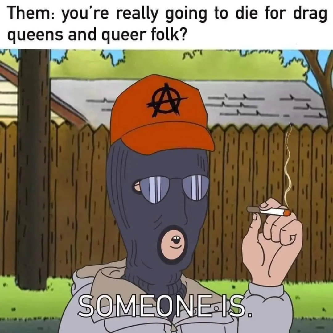 An animated character wearing a black balaclava, sunglasses, and an orange cap with an anarchist symbol smokes a cigarette…