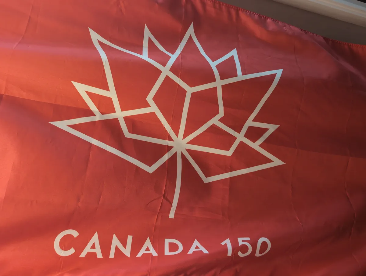 A red fabric banner displays a stylized white maple leaf outline with the text 'CANADA 150' printed below it, referencing…