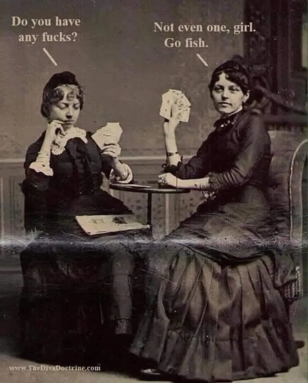 Two women in vintage 19th-century dresses sit at a small table playing cards. The woman on the left looks down at her hand…