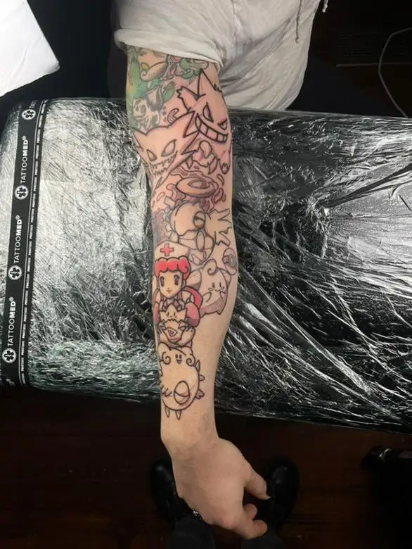 A person's tattooed forearm and upper arm are shown, covered in colorful Pokémon characters including Gengar, Pikachu, and…