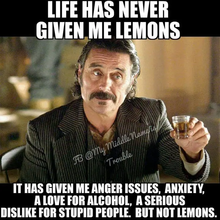 A man with a mustache and a pinstripe suit holds a glass of amber liquid while looking upward with a skeptical expression…