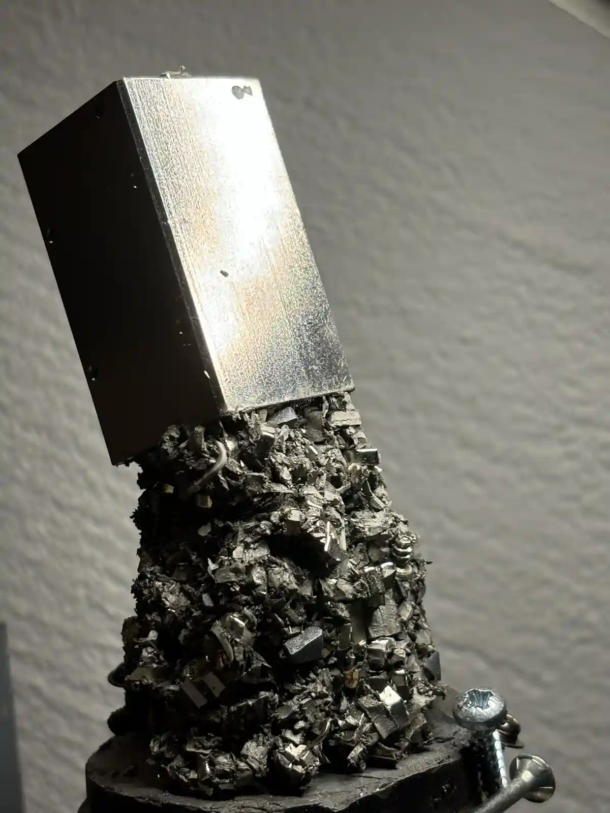 A close-up photo shows a rectangular metal box perched atop a jagged, crystalline pile of dark metallic fragments…