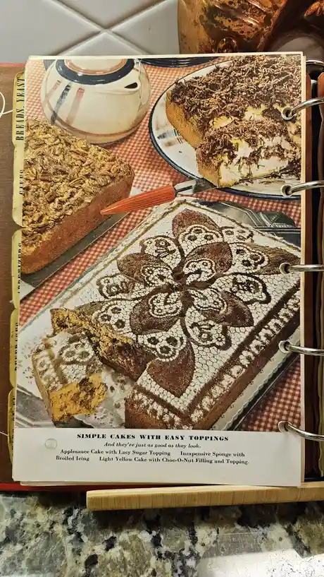 A vintage cookbook page titled 'SIMPLE CAKES WITH EASY TOPPINGS' is shown in a binder, featuring photos of cakes with…