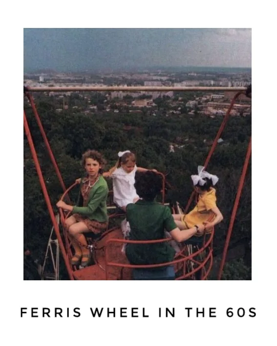 A vintage photograph shows four children in a red, open-air Ferris wheel gondola overlooking a sprawling cityscape with…