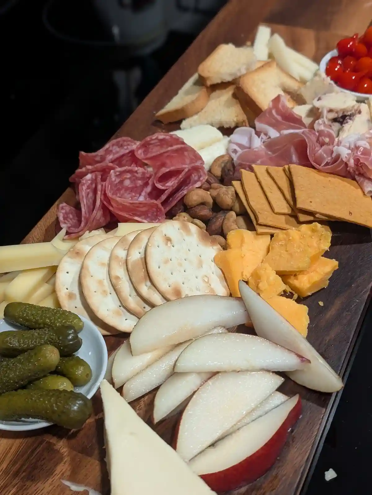 A wooden charcuterie board is filled with an abundant variety of food including sliced salami, prosciutto, assorted cheeses…
