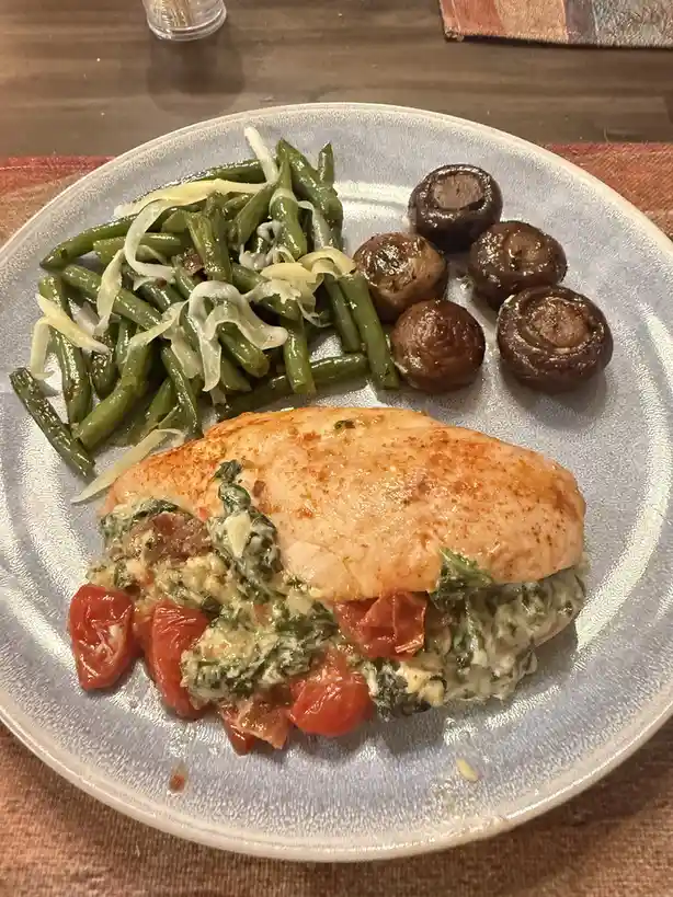A plated meal featuring a stuffed chicken breast with spinach and tomato filling, accompanied by green beans topped with…