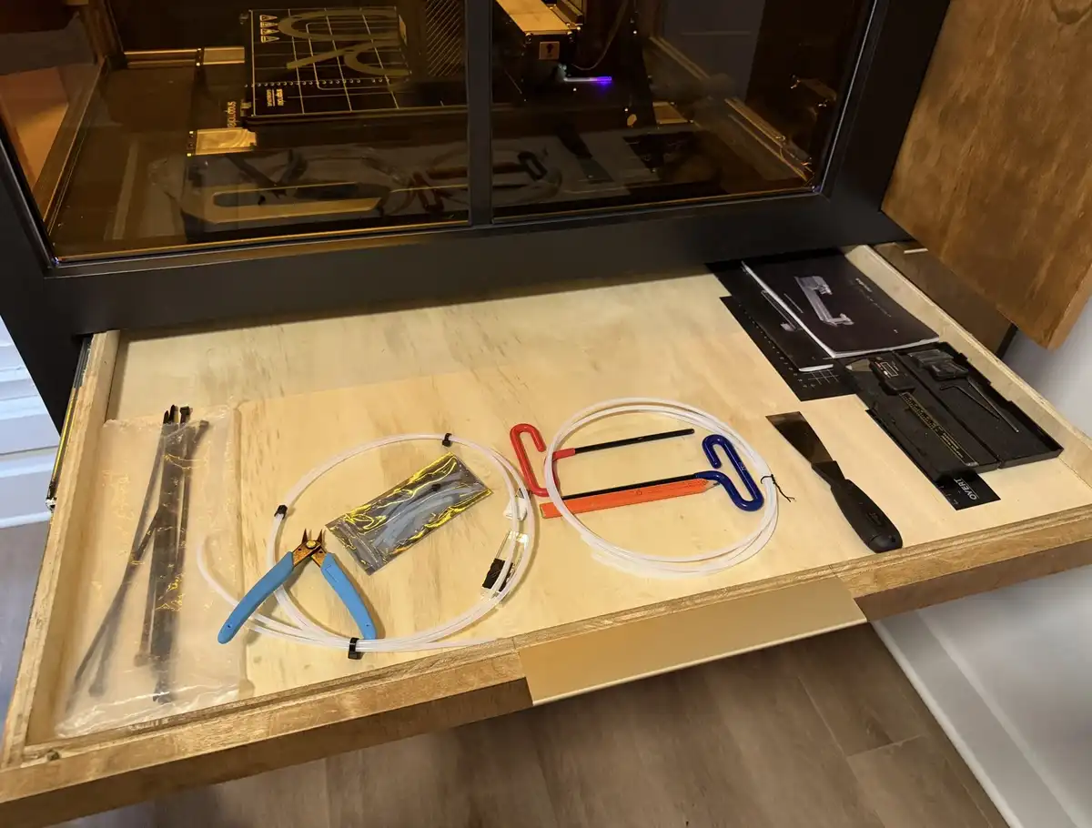 A wooden drawer is pulled open, revealing an organized collection of 3d printer tools and parts including tubing, pliers…