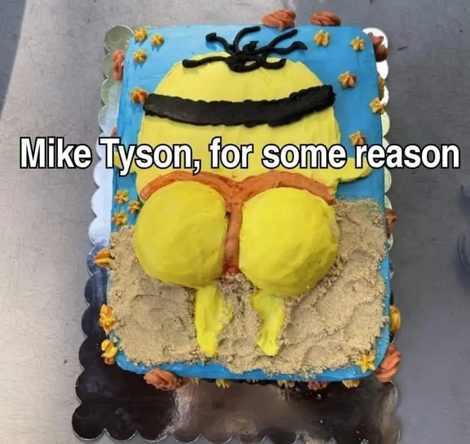 A rectangular cake decorated to resemble a Minion from Despicable Me, viewed from behind, sitting in sand with a blue…