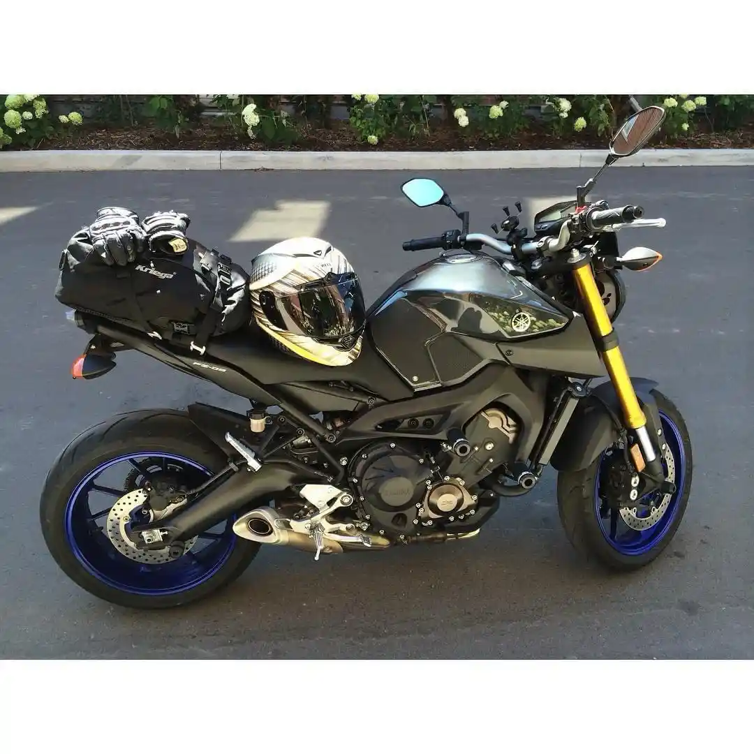 A black Yamaha motorcycle with blue rims and gold front forks is parked on asphalt, with a helmet and gloves resting on its…