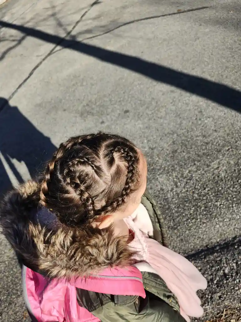 An overhead shot of a young child with dark hair styled in two braids that cross over the top of their head, wearing a pink…