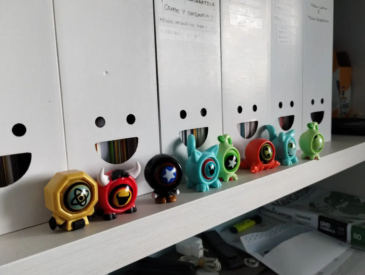 A row of colorful, cartoonish figurines sits on a shelf in front of white filing cabinets with cut-out smiley faces. The…