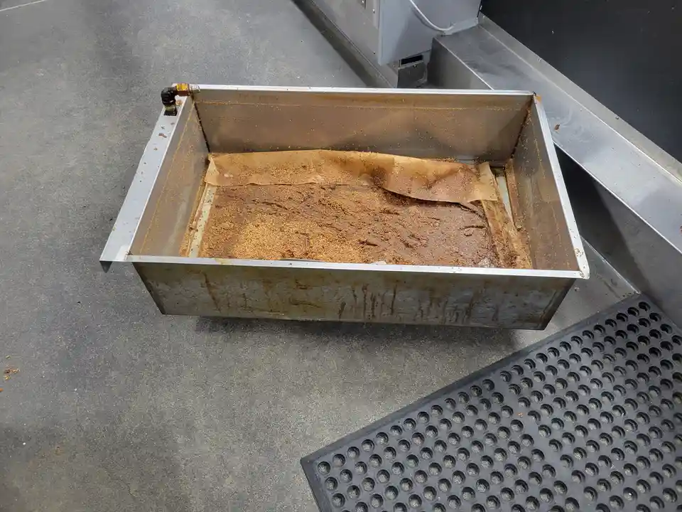 A stainless steel tray, likely for coffee grounds, is filled with brown, gritty residue and a stained paper filter. The tray…