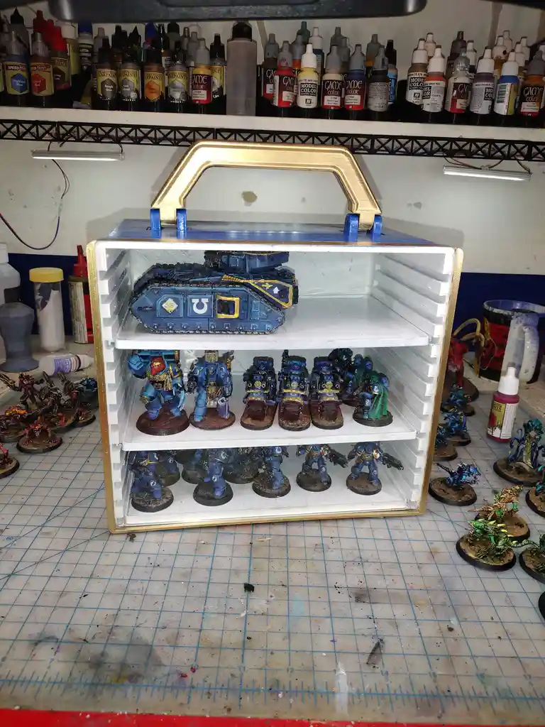 A custom-made, fridge-like display case with a gold handle and white interior holds a collection of painted Warhammer 40,000…