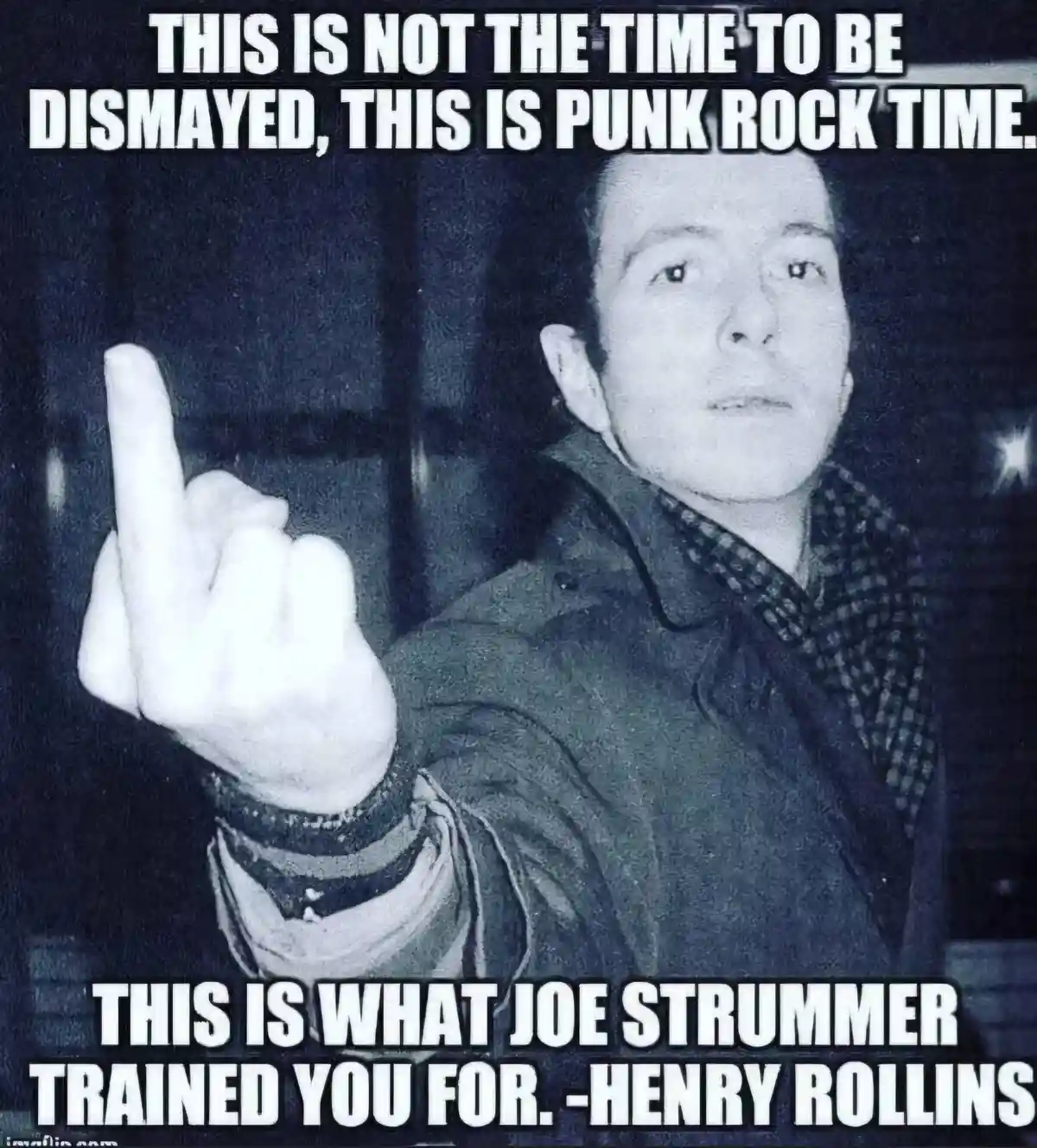 A black-and-white photo shows a man in a jacket and plaid shirt pointing his middle finger forward with a serious…