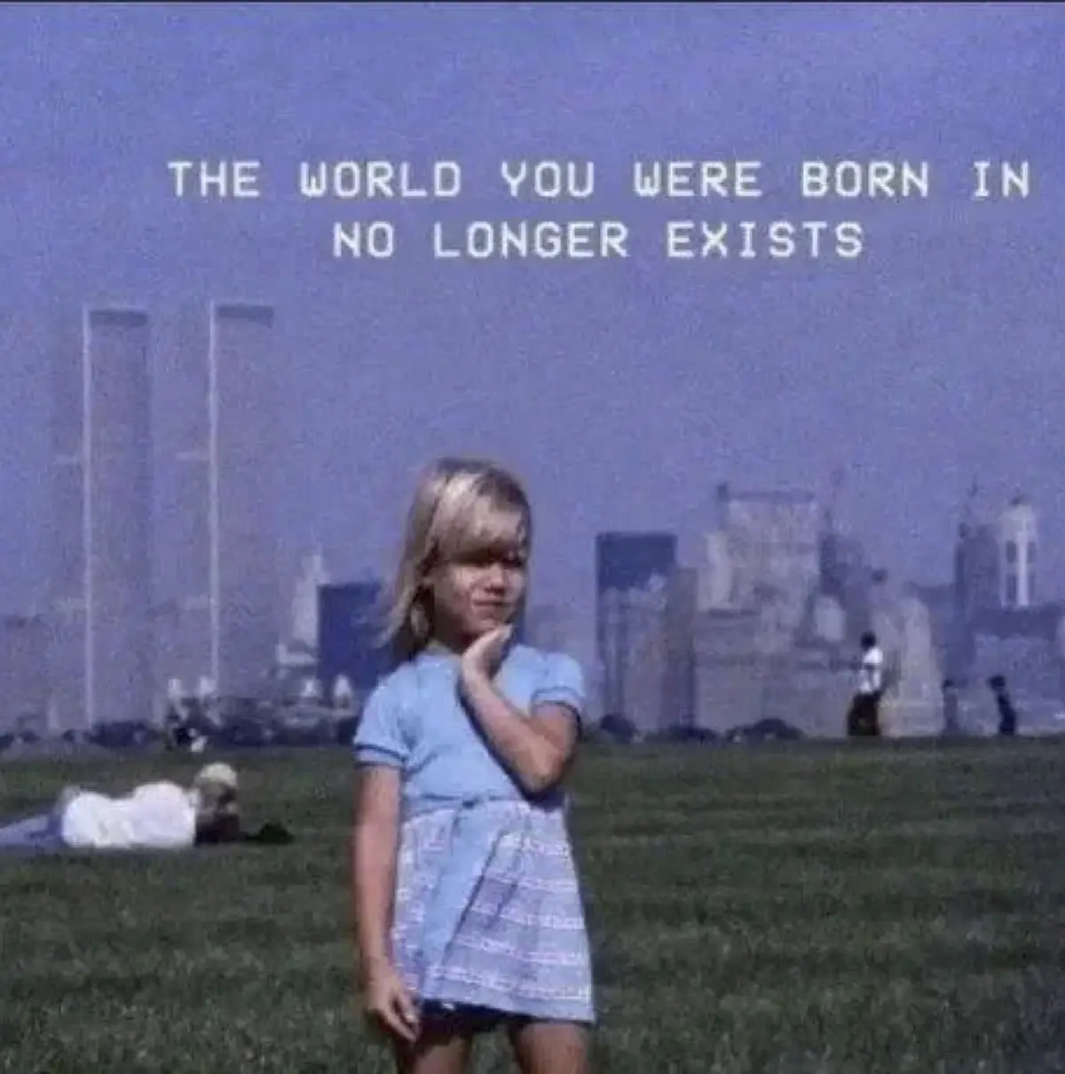 A vintage photo shows a young blonde girl in a blue dress standing on a grassy field, with the Twin Towers of the World…