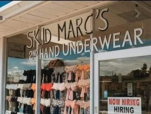 A storefront window displays racks of secondhand underwear with the sign 'SKID MARC'S 2ND HAND UNDERWEAR' above. A 'NOW…